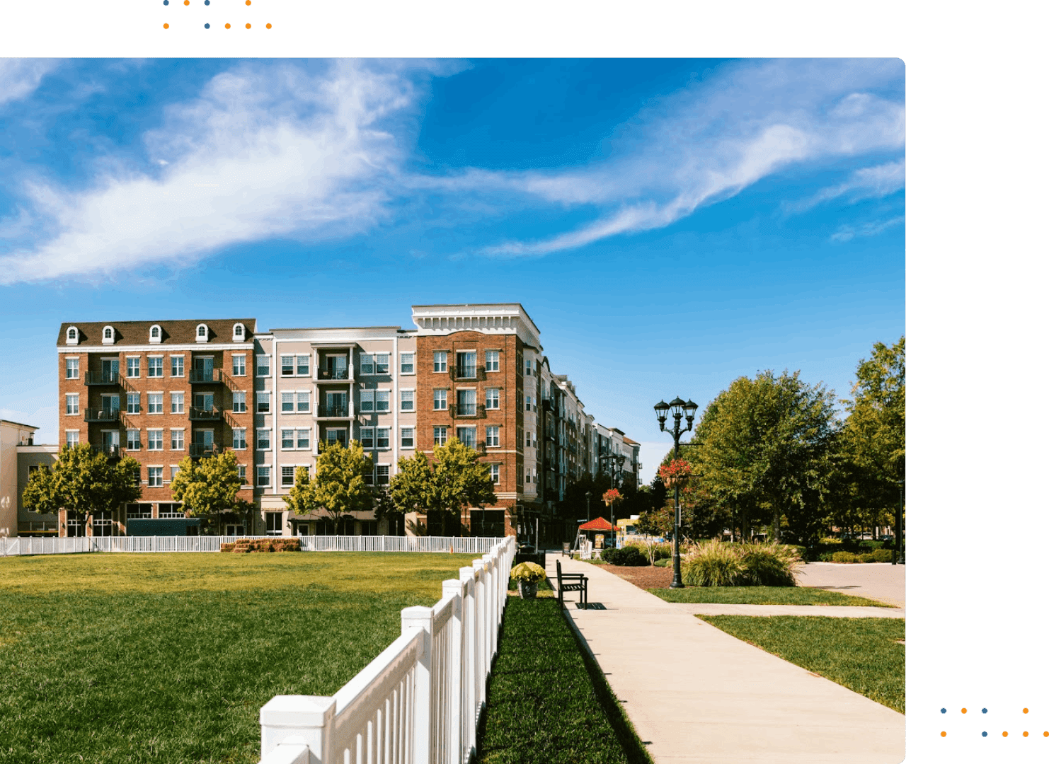 A brick apartment complex with a white fence and green lawn under a blue sky.